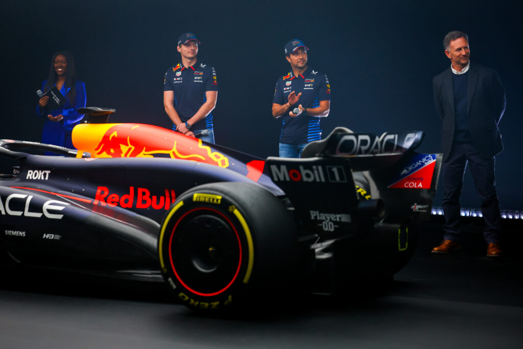 Red Bull Formel-1 Auto. Dahinter Max Verstappen und drei weitere Menschen